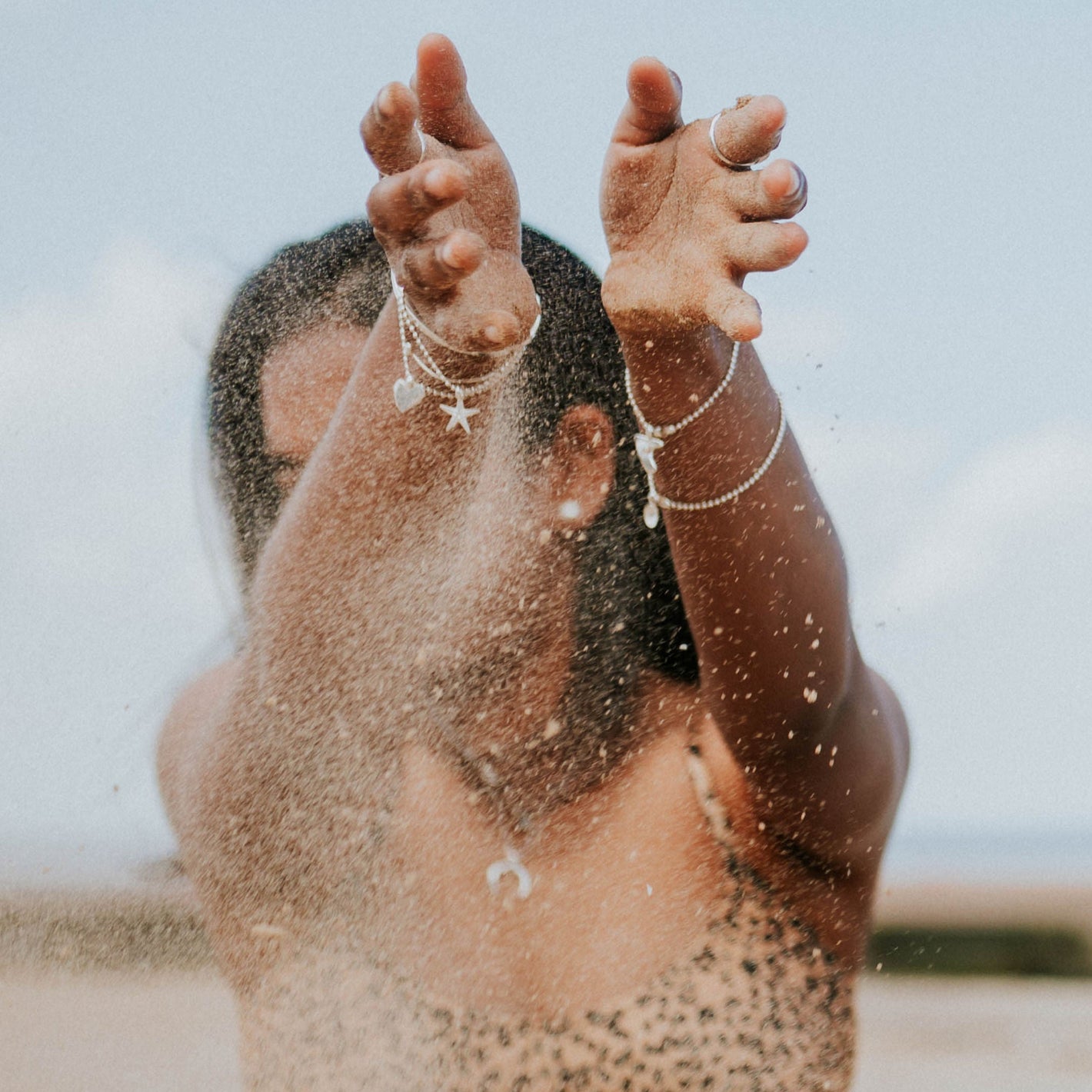Woman wearing multiple bracelets with sand running through her hands, used in bracelet size guide.