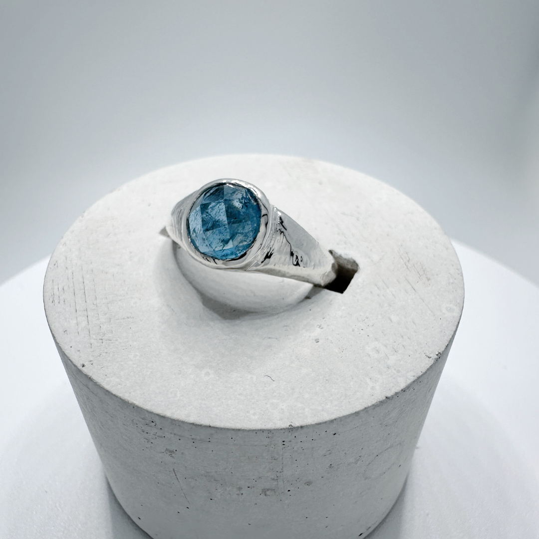 Side view of a sterling silver aquamarine signet ring with natural inclusions in a contemporary concrete ring display holder.