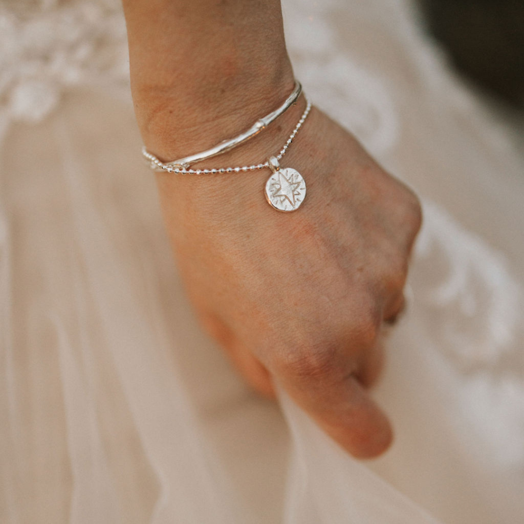 Sterling silver North Star bracelet worn on the wrist with the hand resting against a white wedding dress.