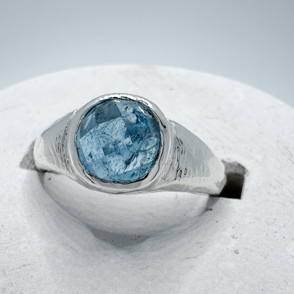 Front view of a sterling silver aquamarine signet ring showing natural gemstone details in a contemporary concrete ring holder.