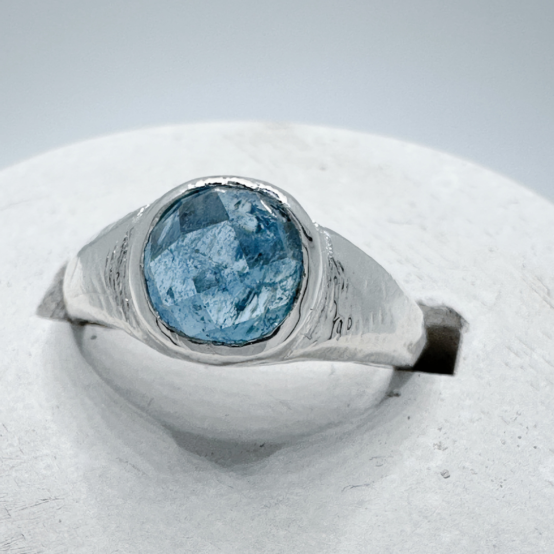 Front view of a sterling silver aquamarine signet ring showing natural gemstone details in a contemporary concrete ring holder.