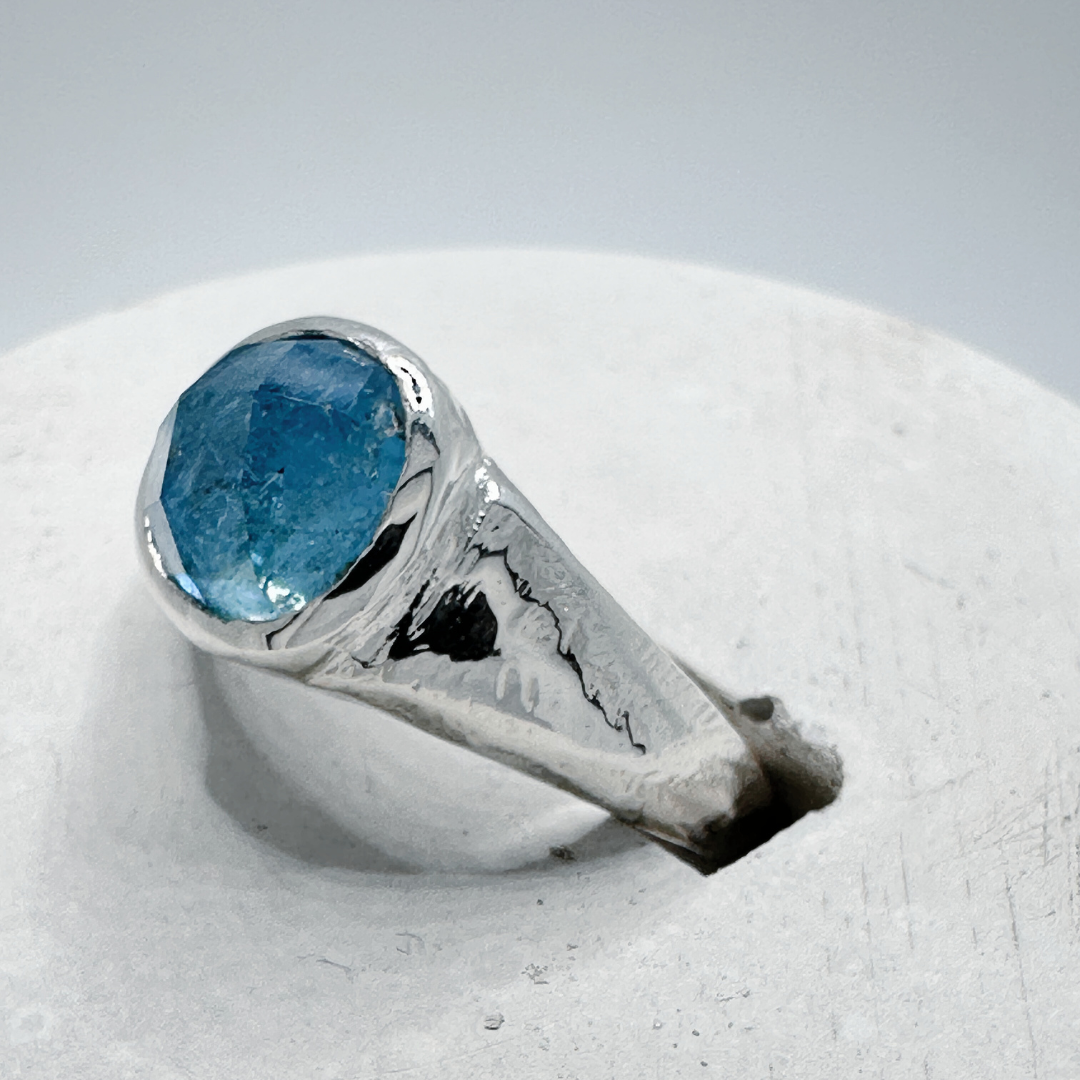 Close up side view of a sterling silver aquamarine signet ring displayed in a contemporary concrete ring holder.
