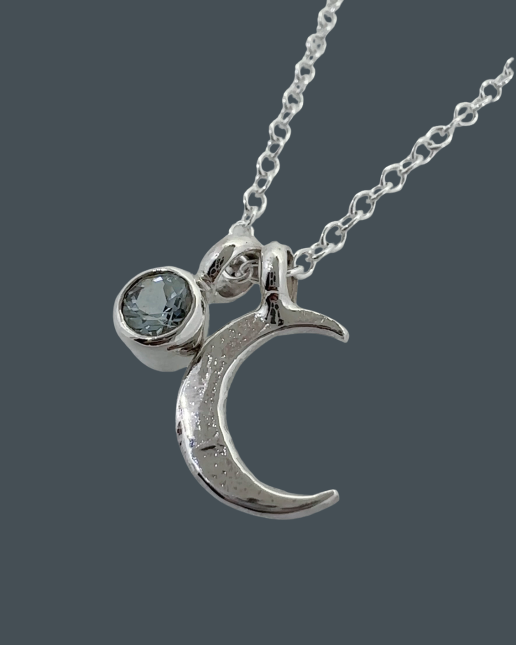 Side-angle close-up of the sterling silver crescent moon necklace with 5mm aquamarine charm showing carving and texture.