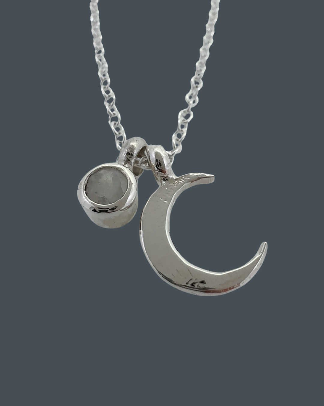 Side-angle close-up of the sterling silver crescent moon necklace with a 5mm moonstone charm showing carving and texture.