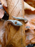Close-up of a sterling silver snake ring set with a citrine stone in the head, photographed with autumnal orange leaves in the background.