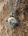 Close-up of a sterling silver Uruz rune charm with carved rune detail and a rugged, relic-like texture on a sand background.