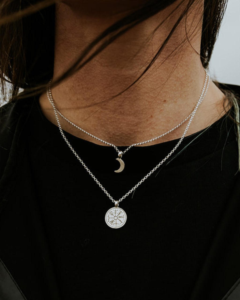 Sterling silver Vegvisir necklace layered with a small crescent moon necklace worn over black clothing.