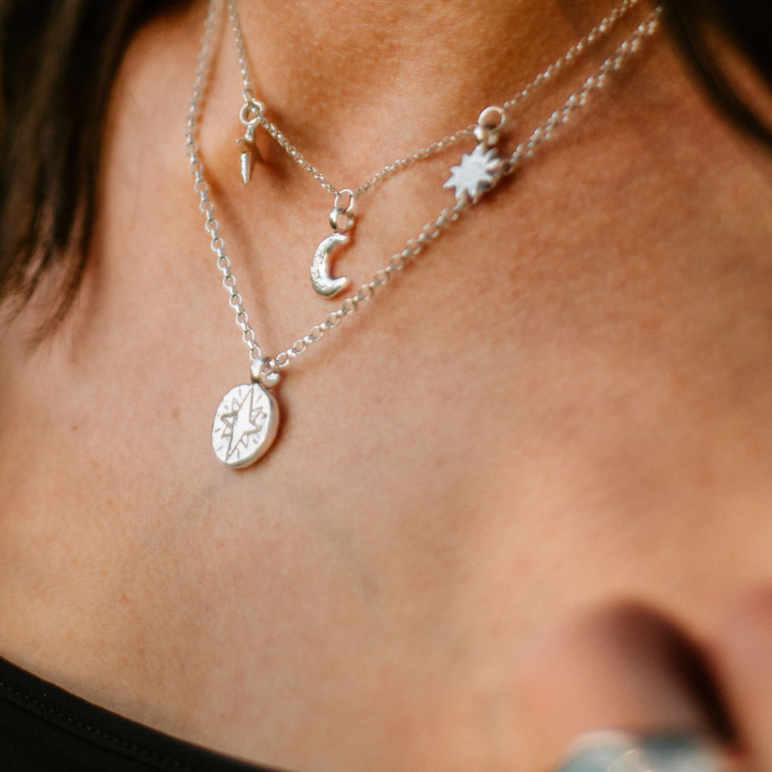 Close-up of layered sterling silver necklaces: North Star pendant and Sun, Moon and Stars necklace, with blurred amazonite ring.