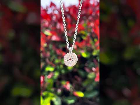 Recycled silver North Star necklace customised with garnet January birthstone, filmed beside a red robin tree to reflect its vibrant, grounding energy.