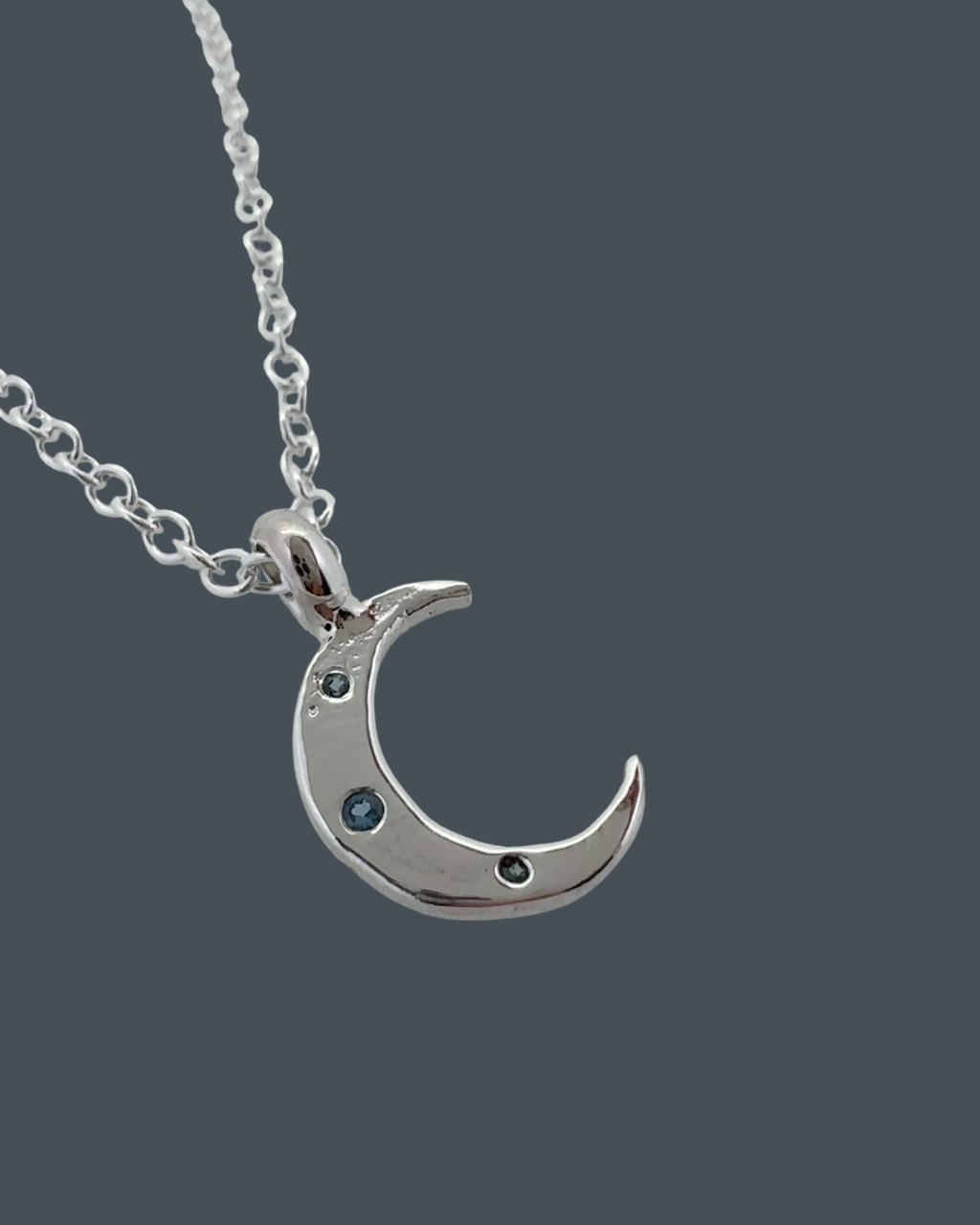 Side angle of handcrafted silver crescent moon necklace highlighting organic curves and raw, sand-cast texture.