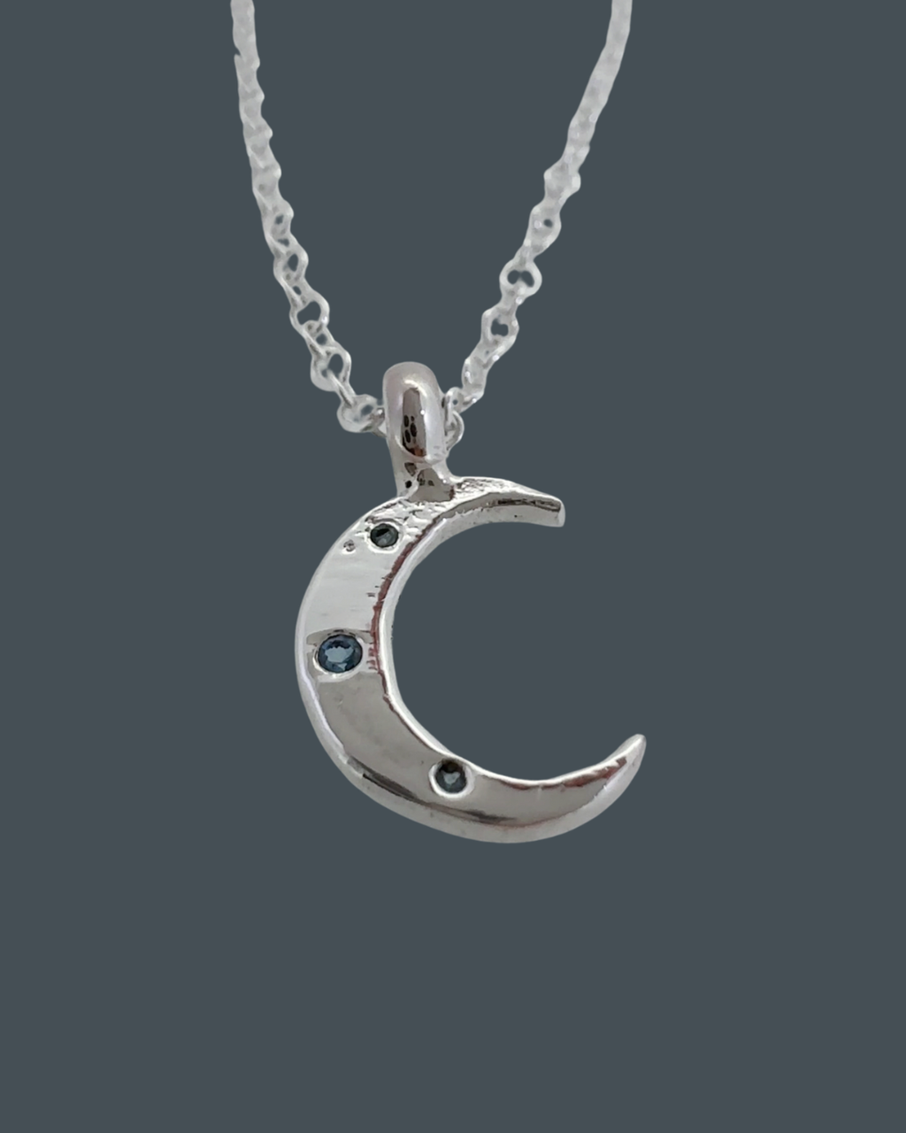 Silver crescent moon necklace with three aquamarines, handcrafted in recycled sterling silver, front view on blue/grey background.